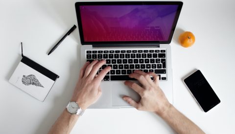 Hands typing on a silver laptop